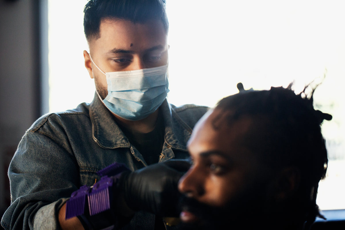 Barber cutting a client's hair while another customer waits for his turn on a bench